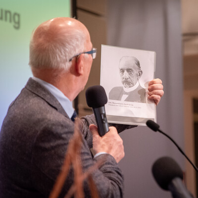 Kammerpr&auml;sident Gerhard Schwetje zeigt w&auml;hrend des Gesellschaftsabends 2025 ein Bildnis von John C. Funch, der vor 125 Jahren, am 20.11.1900, zum ersten Pr&auml;sidenten der Landwirtschaftskammer Weser-Ems gew&auml;hlt worden war.