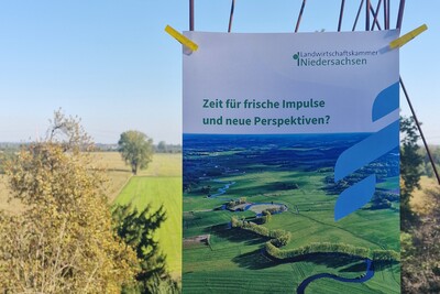 Ein Plakat der Landwirtschaftskammer Niedersachsen h&auml;ngt vor einer l&auml;ndlichen Landschaft mit B&auml;umen und Feldern.