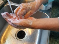 Eine Person wäscht sich die Hände mit Seife unter fließendem Wasser in einem Waschbecken.