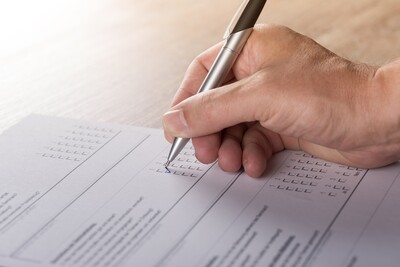 Eine Hand f&uuml;llt mit einem Stift ein Formular oder einen Fragebogen auf einem Holztisch aus.