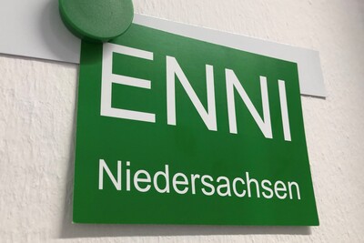 Gr&uuml;nes Schild mit der Aufschrift ENNI Niedersachsen, befestigt mit einem gr&uuml;nen Magneten an einer wei&szlig;en Wand.