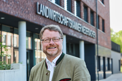 Ein Mann mit Brille und Bart steht l&auml;chelnd vor einem Geb&auml;ude mit der Aufschrift "Landwirtschaftskammer".