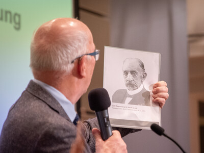 Kammerpr&auml;sident Gerhard Schwetje zeigt w&auml;hrend des Gesellschaftsabends 2025 ein Bildnis von John C. Funch, der vor 125 Jahren, am 20.11.1900, zum ersten Pr&auml;sidenten der Landwirtschaftskammer Weser-Ems gew&auml;hlt worden war.