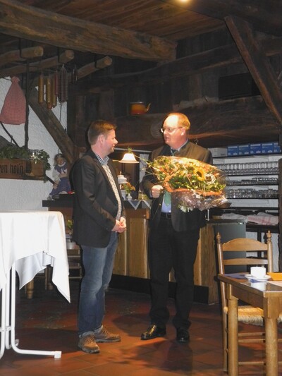 Nach seiner Rede gratuliert der stellv. Präsident der Landwirtschaftskammer Niedersachsen, Heinrich Grupe, dem Preisträger - © Dr. Hans-Gerd Brunken Zwei Männer stehen in einem rustikalen Raum. Einer überreicht dem anderen einen Blumenstrauß.