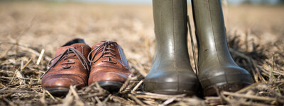 - © Wolfgang Ehrecke Ein Paar braune Lederschuhe und grüne Gummistiefel stehen auf einem Feld mit Stroh.
