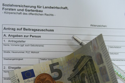 Formular der Sozialversicherung f&uuml;r Landwirtschaft mit Euro-M&uuml;nzen und einem 5-Euro-Schein darauf. Ein Stift liegt daneben.