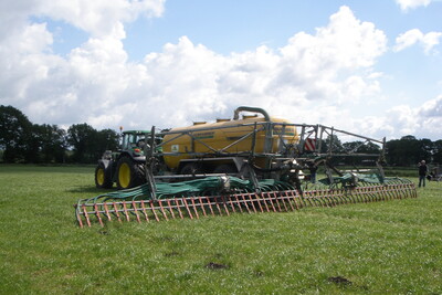 Traktor mit gro&szlig;em gelbem Tankanh&auml;nger und Verteiler auf einem gr&uuml;nen Feld unter bew&ouml;lktem Himmel.