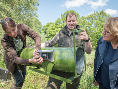 LWK-Nutriaj&auml;gerin Johanne van Scharrel-Bruns (l.) und LWK-Nutriaj&auml;ger Bj&ouml;rn Matthies (M.) erkl&auml;ren Niedersachsens Landwirtschaftsministerin Barbara Otte-Kinast (r.) die Funktionsweise der vom Ministerium finanzierten Lebendfallen.