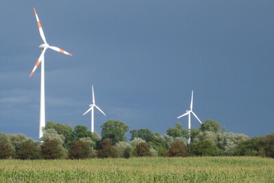 Mehrere Windr&auml;der stehen auf einem Feld vor einem dunklen, bew&ouml;lkten Himmel.