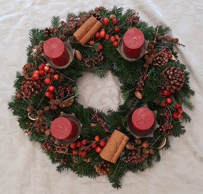 Adventskranz mit vier roten Kerzen, Tannenzweigen, Zimtstangen, Beeren und Tannenzapfen auf wei&szlig;em Tischtuch.