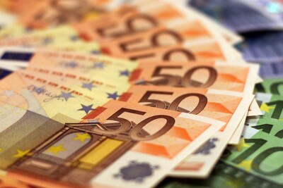 Verschiedene Euro-Banknoten in unterschiedlichen Werten liegen gestapelt und verteilt auf einer Fl&auml;che.